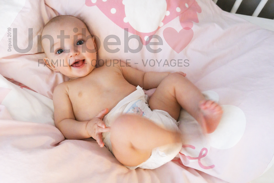 un bébé souriant, allongé dans son lit, porte une couche